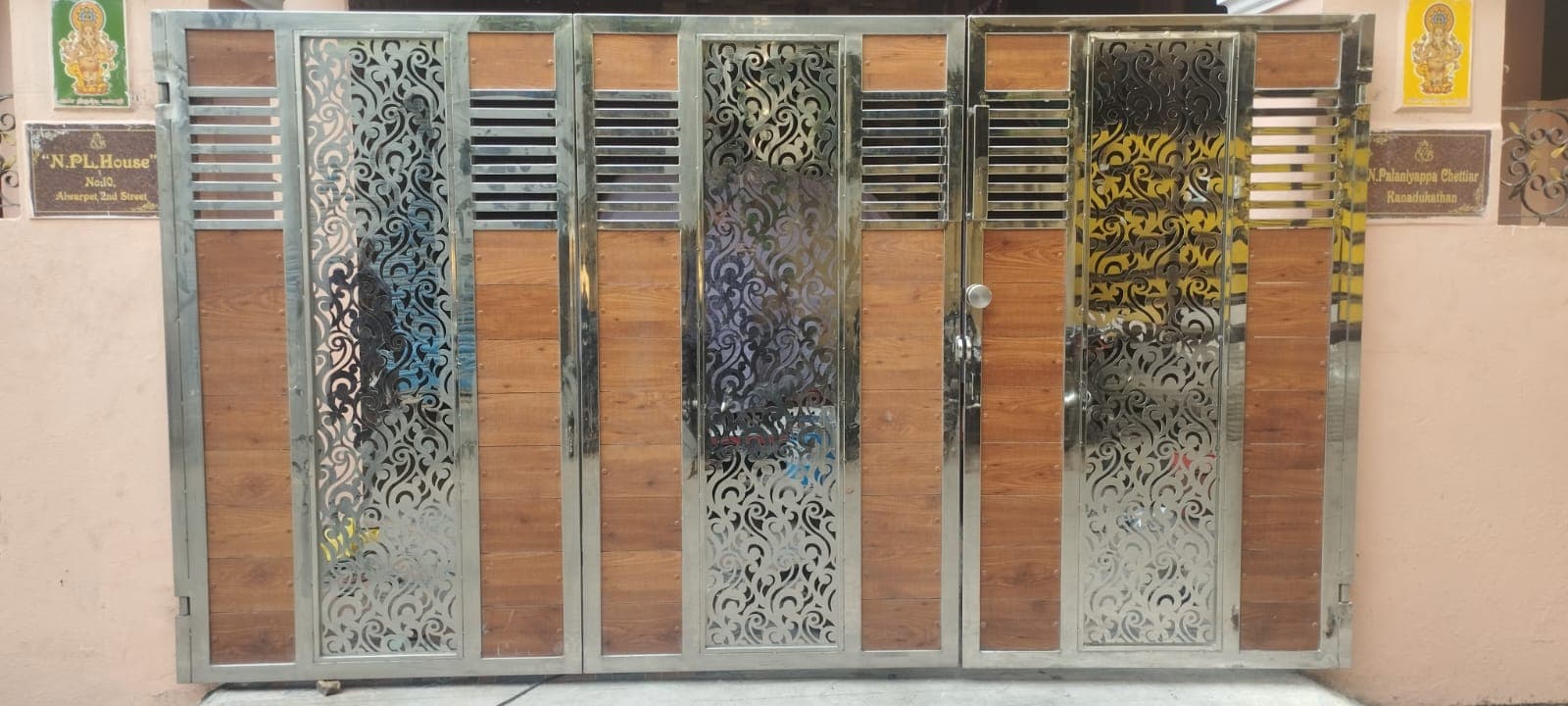 Custom stainless steel and wood-finish bi-folding driveway gate with laser-cut panels